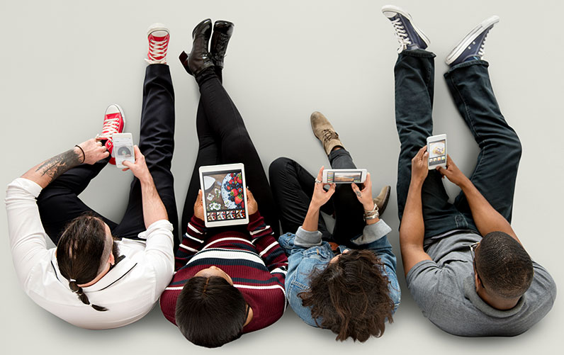 four people sitting on the floor using devices