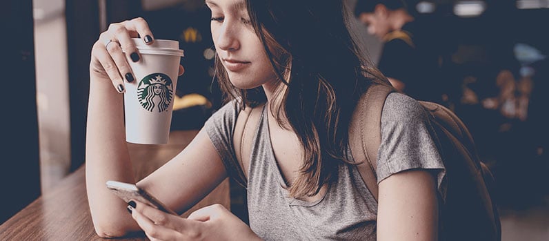 young girl using phone and holding coffee