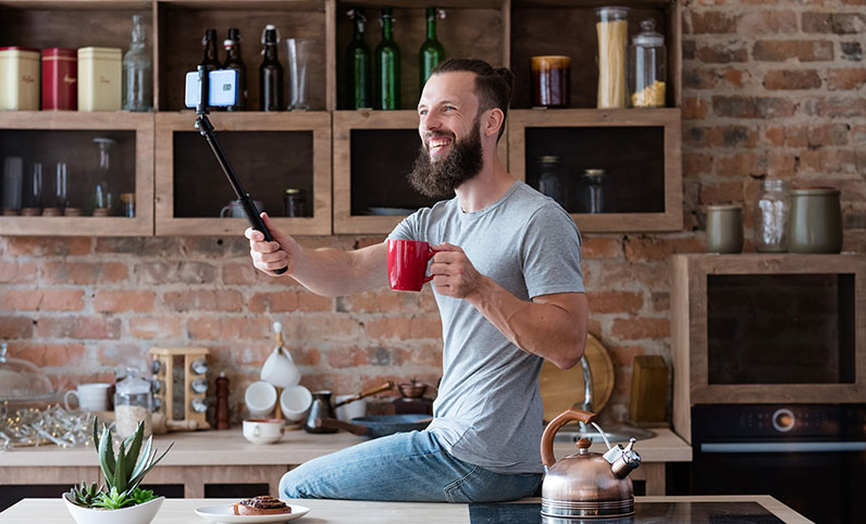 man holding a selfie stick looking at phone and holding cup