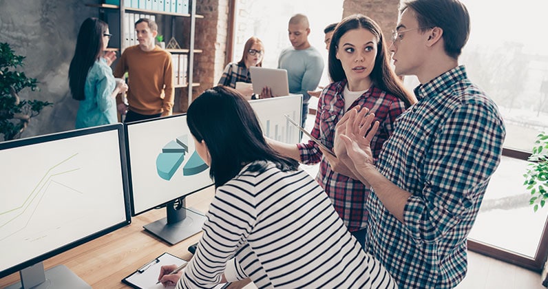 several people in an office talking and looking at computer