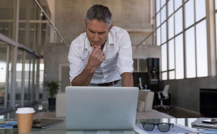 100+ Interview Questions For Executives With Sample Answers Evinex Corporation | Staffing Agency man thinking in front of a laptop