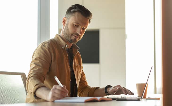 man-writing-pen-using-laptop