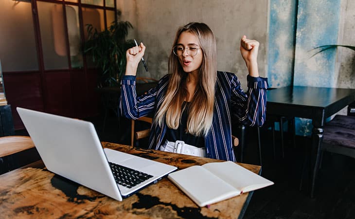 happy woman with her hands in the air using a laptop
