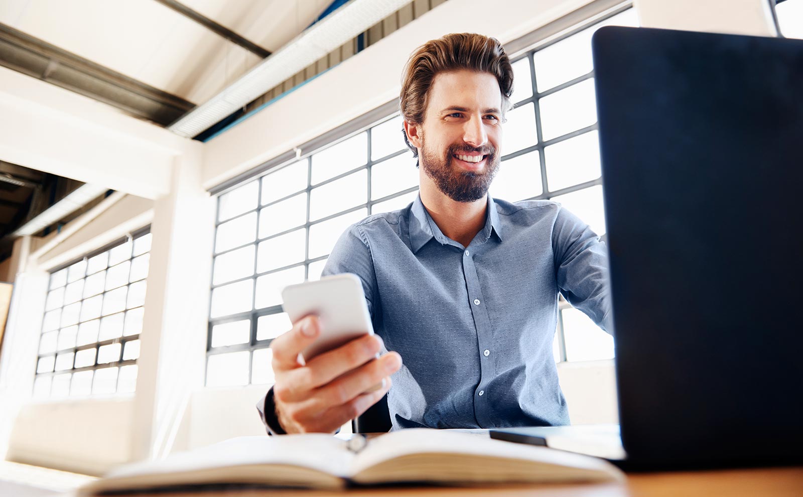 smiling man holding a phone and using a computer