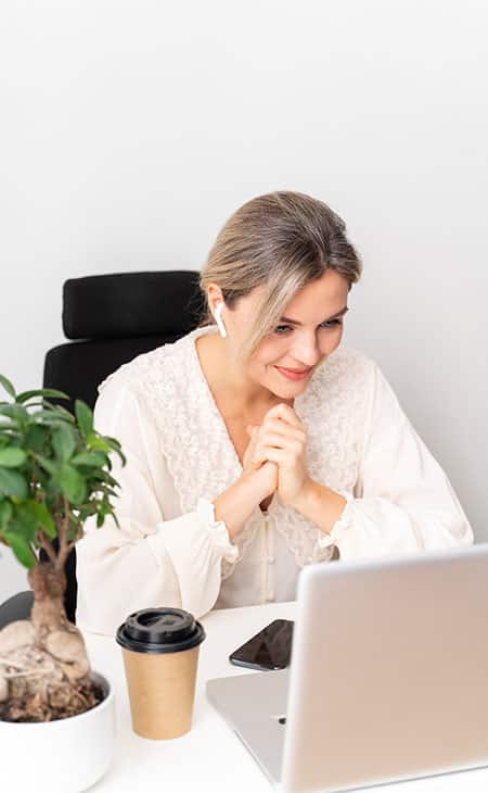woman with her hands together looking at a laptop