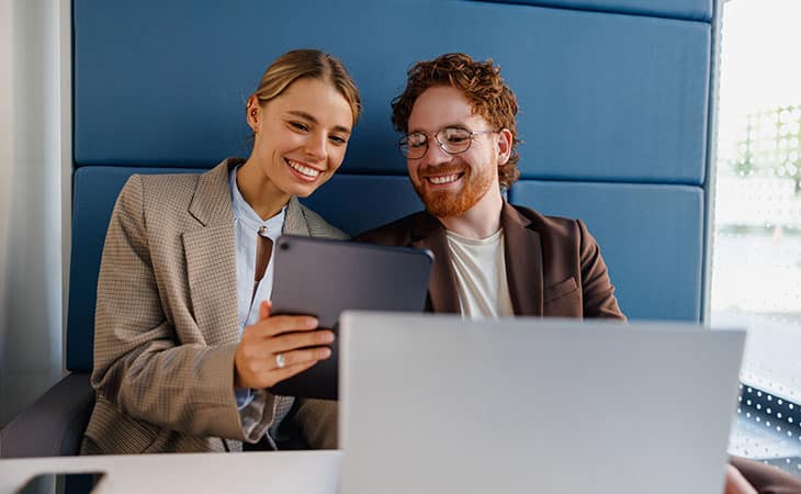 Mastering Interpersonal Skills: Your Guide To Success Evinex Corporation | Staffing Agency a businessman and a businesswoman smiling looking at a tablet