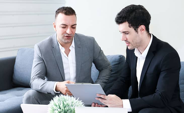 two men having a conversation looking at a clip folder