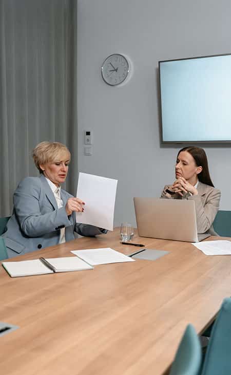 two women talking pointing to papers and using a laptop
