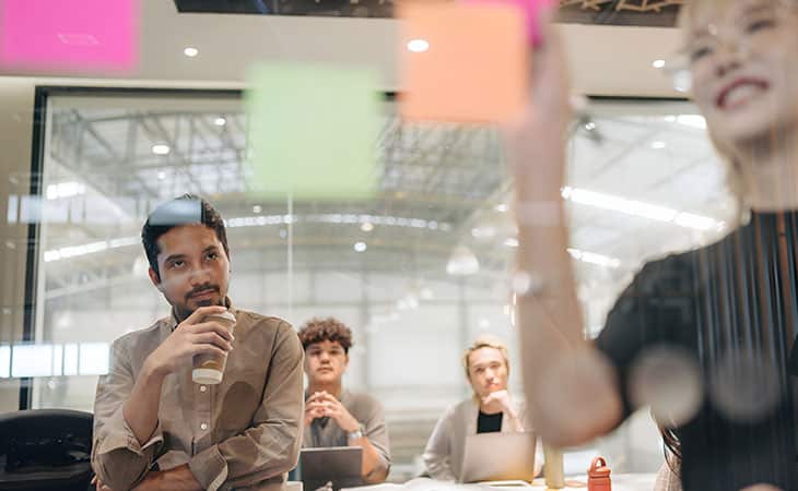 What Is Workforce Management? Key Benefits Evinex Corporation | Staffing Agency a happy woman writing postits while coworkers look
