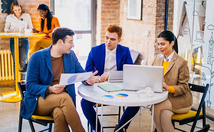 Sales Manager Job Description: Attract And Hire Top Talent Evinex Corporation | Staffing Agency three people at a table and two people in the back of an office
