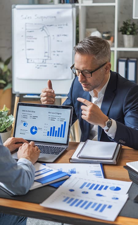 100+ Sales Manager Interview Questions With Answers Evinex Corporation | Staffing Agency a man explaining and making gestures to a colleague that is using a laptop