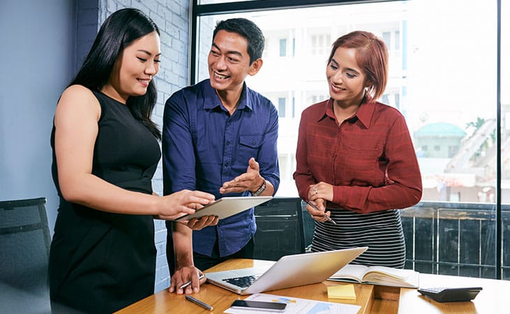 100+ Sales Manager Interview Questions With Answers Evinex Corporation | Staffing Agency three people talking looking at a tablet in an office