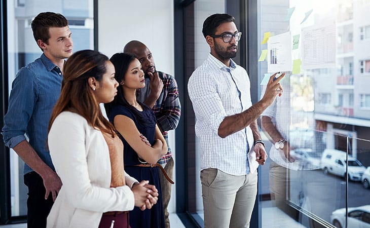 100+ Chief Of Staff Interview Questions. Find Top Leaders Evinex Corporation | Staffing Agency a man explaining and pointing at a glass wall with papers on it