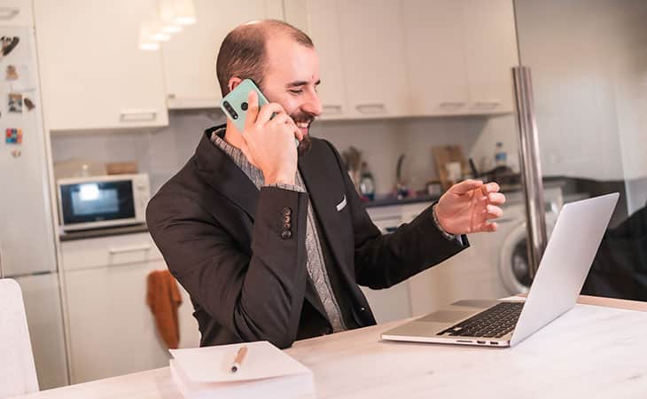 a man with a phone and a laptop is at home
