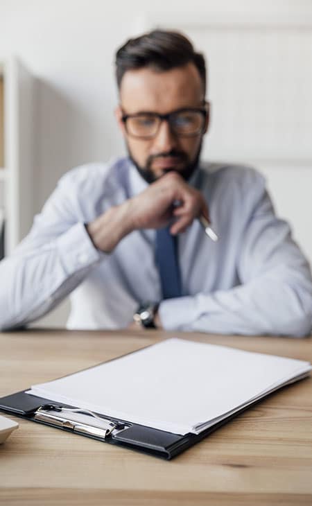 100+ Chief Of Staff Interview Questions. Find Top Leaders Evinex Corporation | Staffing Agency a thoughtful man looking at papers with a pen in his hand