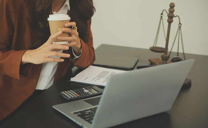 Hr Issues And Challenges: Solutions For The Modern Workplace Evinex Corporation | Staffing Agency a woman holding a coffee while analyzing documents on a computer