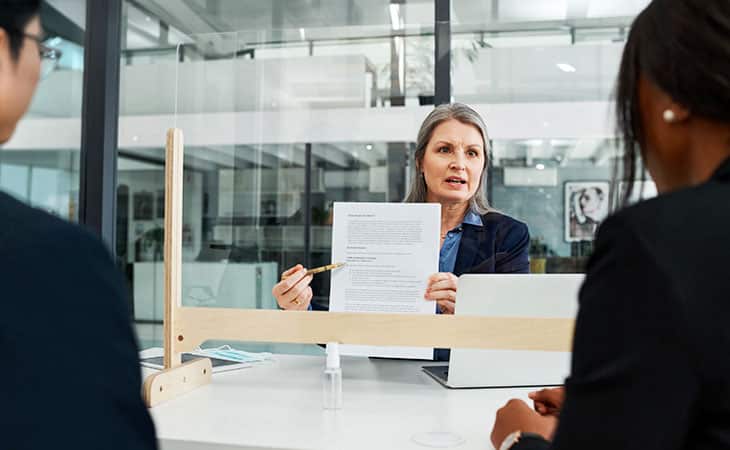 Hr Issues And Challenges: Solutions For The Modern Workplace Evinex Corporation | Staffing Agency a woman presenting a document to two colleagues across a plexiglass divider