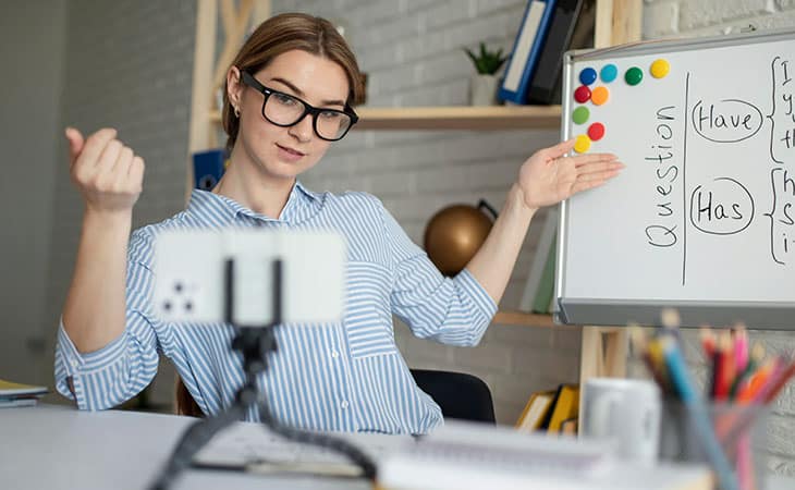 a woman wearing glasses is teaching grammar while pointing at a whiteboard
