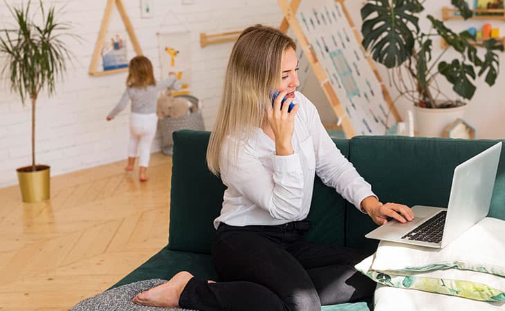 a woman with a phone and a laptop is accompanied by a child