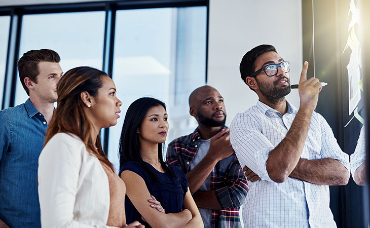 How To Lead A Team: Strategies For Effective Leadership Evinex Corporation | Staffing Agency a man pointing up and explaining something to a group of people