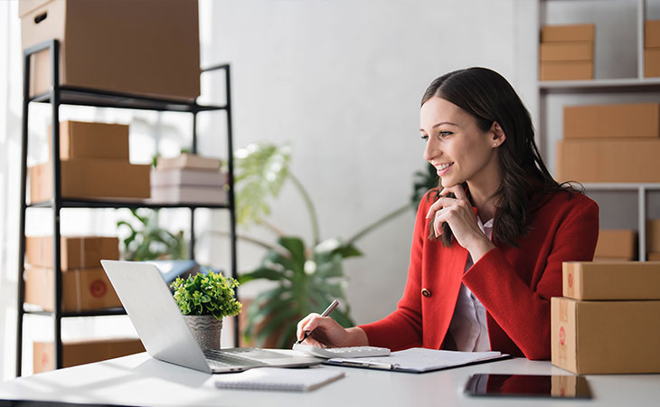 a smiling woman with her hand in her chin while using laptop