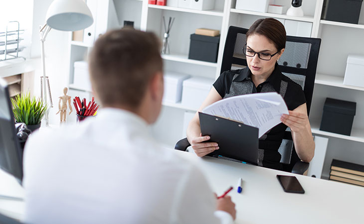 How To Impress In An Interview: Tips To Stand Out Evinex Corporation | Staffing Agency a woman holding and looking at papers while interviewing a candidate